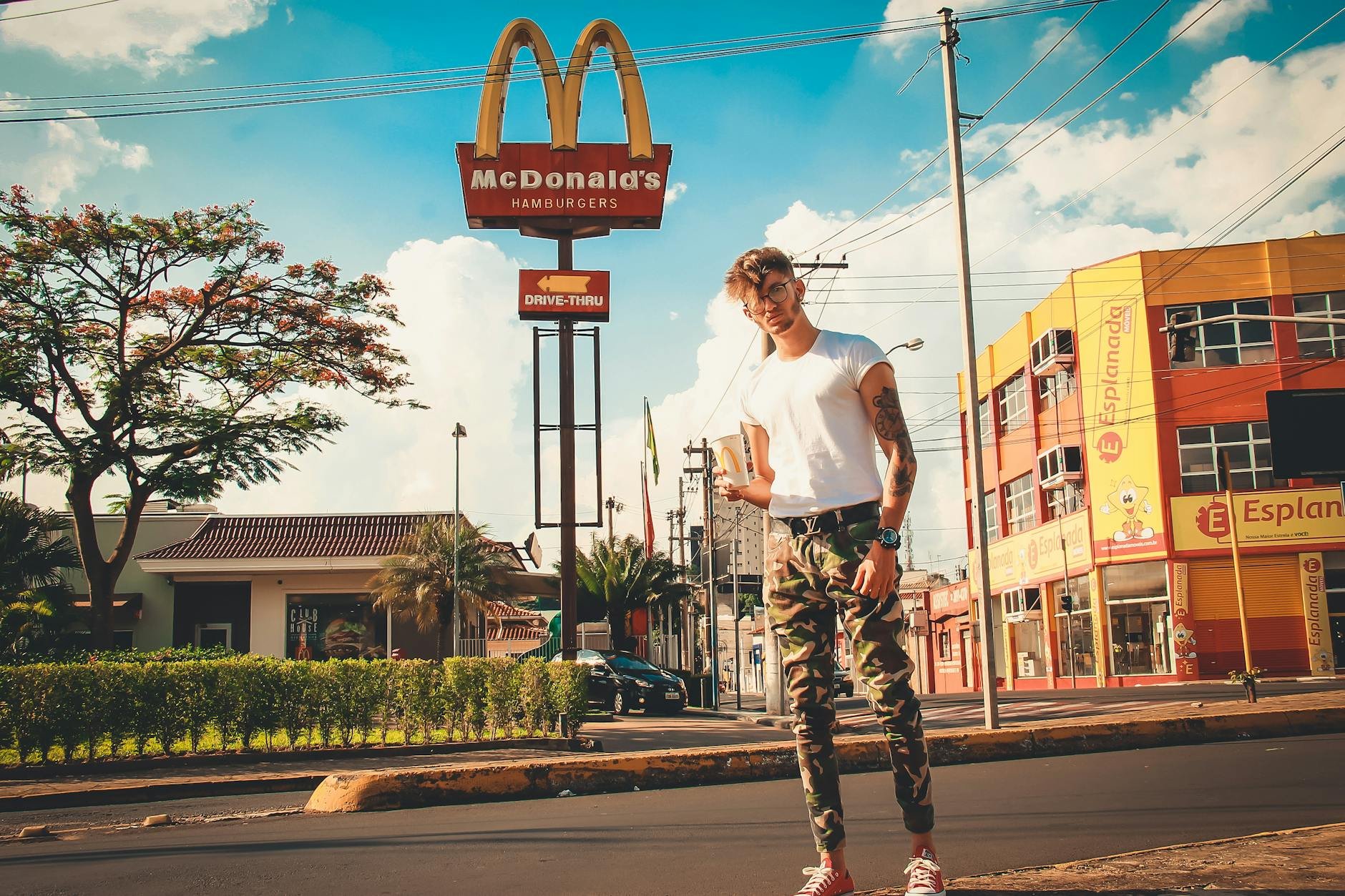 Homem estiloso em área urbana perto de placa do McDonald's ao sol, referência visual para falar de preço