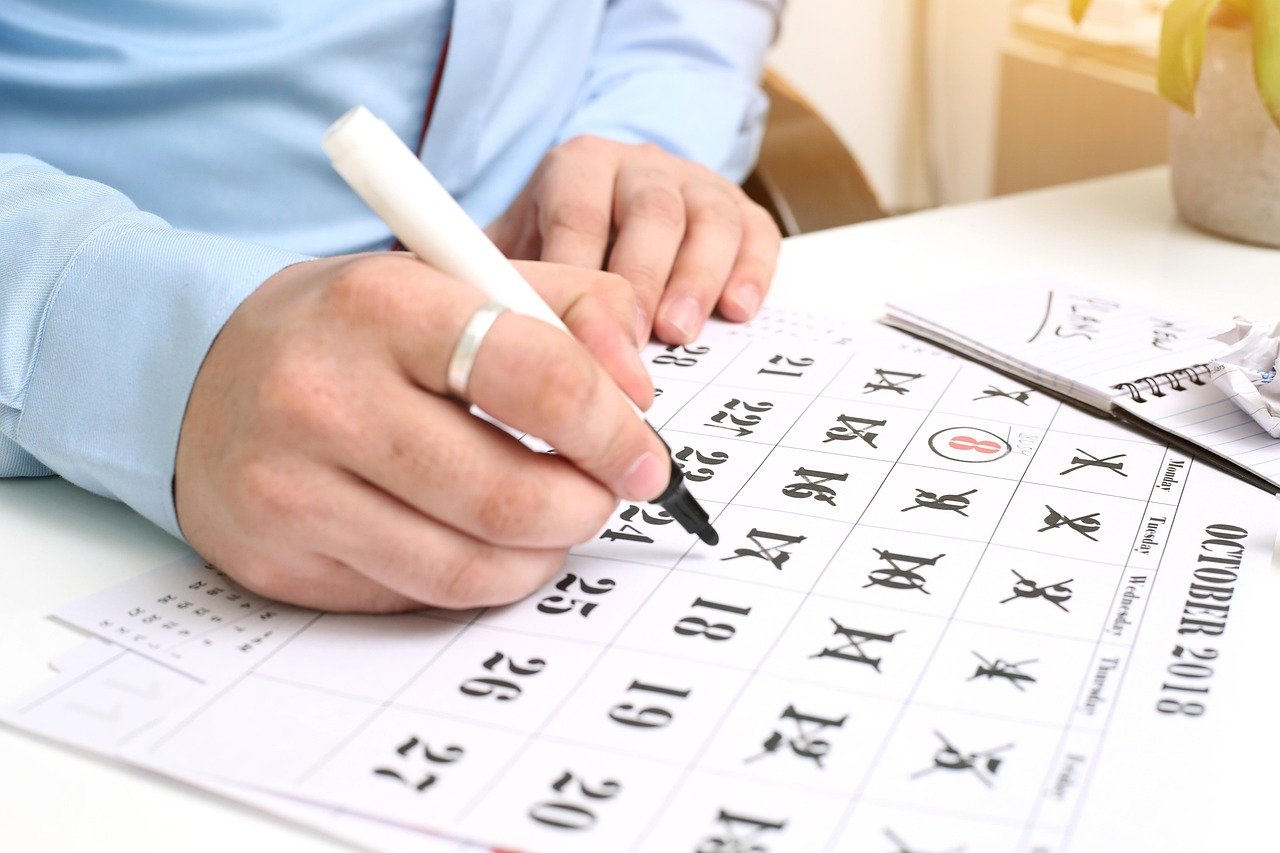 Mão marcando datas em calendário para planejar cadência e jornadas de campanhas de engajamento